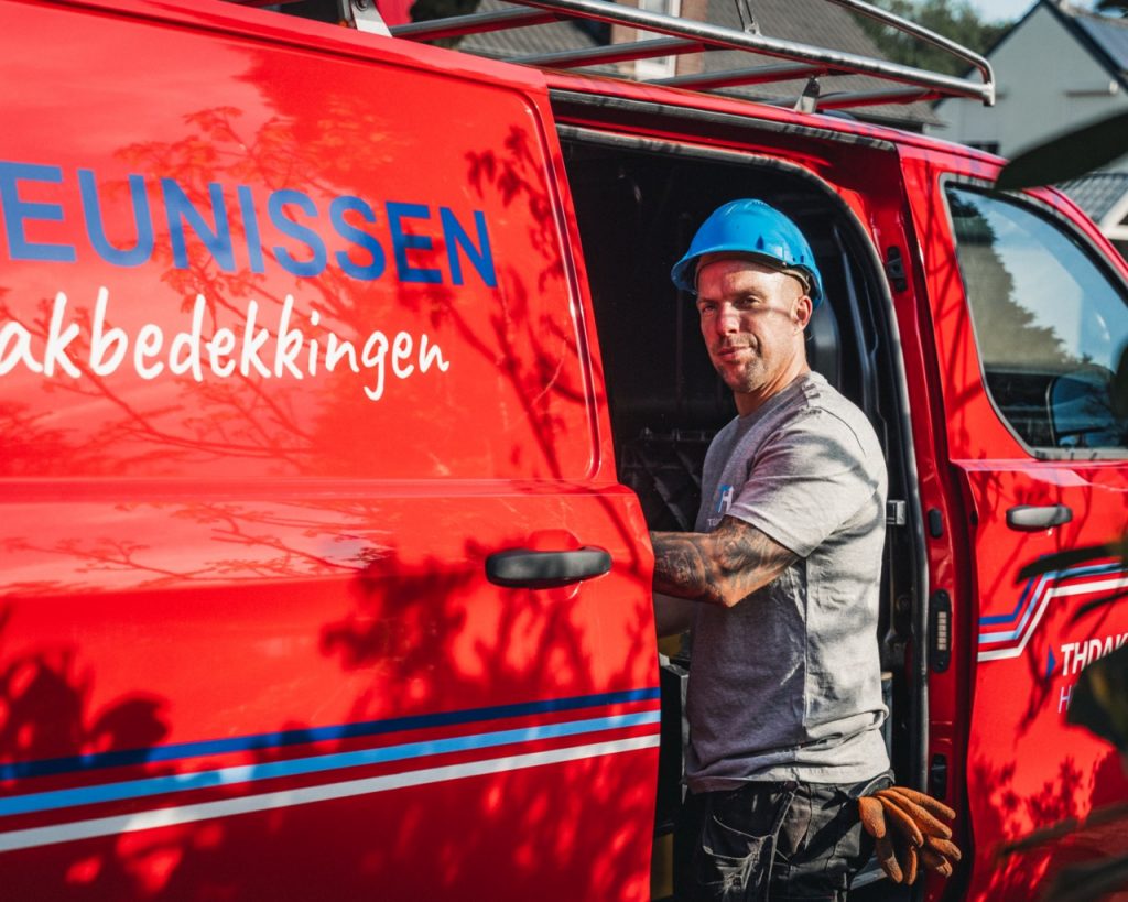 Dakdekker staat bij de werkbus kijkend in de camera